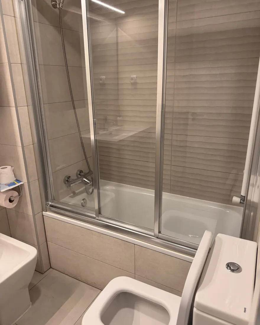 Baño con mampara de cristal y sanitarios blancos, recién limpiado